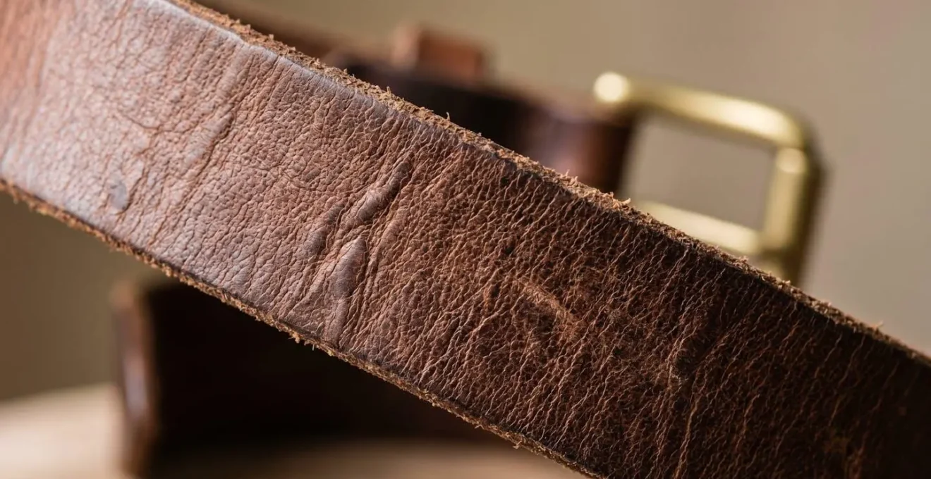 Détail macro d'une ceinture en cuir pleine fleur montrant la texture naturelle et la qualité artisanale